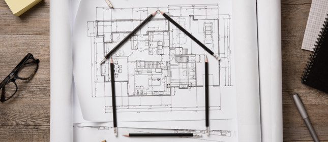 Top view of architectural blueprints, rolls and drawing instruments on the worktable. Shape of house with black pencils on a project house. Architectural drawings with house keys on wooden table, new home concept.