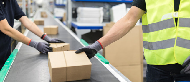 Workers working on conveyor belt in packaging plant. Working for Online-Shopping: Cropped shot of worker hands takes parcel from moving belt conveyor at distribution warehouse.