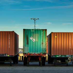 Rear view of a line of trucks loaded with differently colored shipping containers.